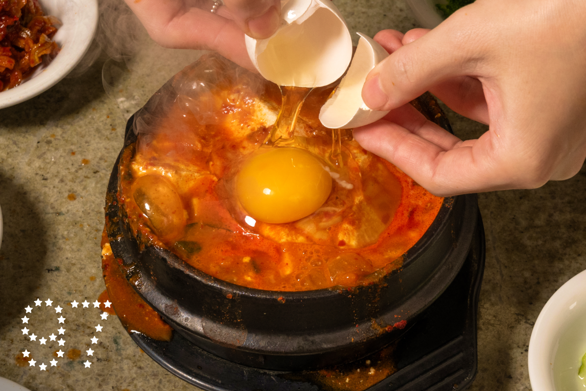 LOS ANGELES, CA - OCTOBER 28, 2024: A raw egg is dropped into a bubbling cauldron of kimchi soontofu surrounded by banchan at Surawon Tofu House in Los Angeles. (Ron De Angelis / For The Times)