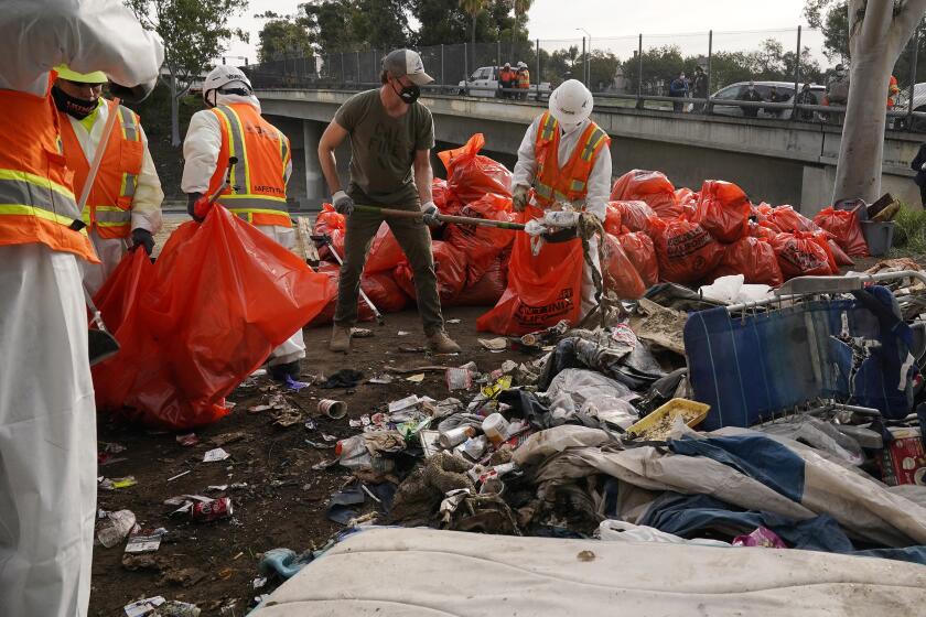 FILE - California Gov. Gavin Newsom, center, helps clean a homeless encampment alongside a freeway on Jan. 12, 2022, in San Diego. Newsom issued an executive order Thursday, July 25, 2024, for the removal of homeless encampments in the state. (AP Photo/Gregory Bull, File)