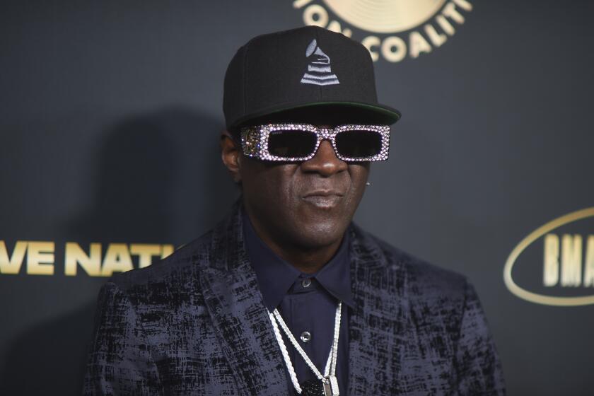 Flavor Flav poses in dark suit jacket, sequined sunglasses, and Grammys hat at the 2024 Black Music Action Coalition Gala