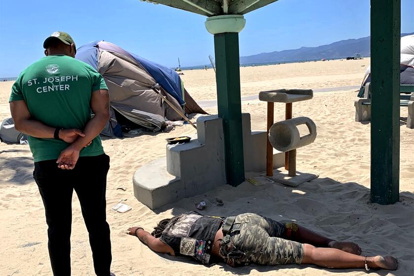 VENICE BEACH, CALIF. - JUNE 23, 2021 - Dawan Moses, director of outreach teams at St. Joseph Center, checks on a woman lying in the sand in late June. (Carla Hall / Los Angeles Times)