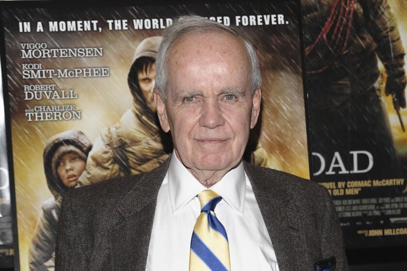 Author Cormac McCarthy poses in a suit in front of a movie poster