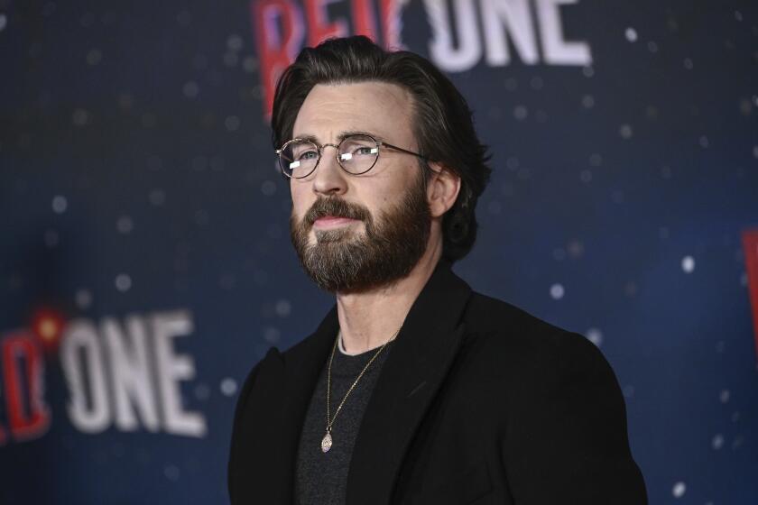 A bearded Chris Evans wearing glasses and a black t-shirt and blazer poses for photos at a red-carpet premiere