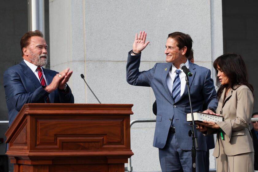 Los Angeles, CA - December 03: Nathan Hochman, center, is sworn in by Arnold Schwarzenegger, left, alongside his wife Vivienne Vella as the new LA County District Attorney after beating out George Gascon in last monthOs election at Hall of Justice on Tuesday, Dec. 3, 2024 in Los Angeles, CA. (Robert Gauthier / Los Angeles Times)